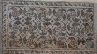 Roman mosaic panel filled with interlaced quatrefoil motifs in gray, cream, black, and muted red, edged by a meander border.