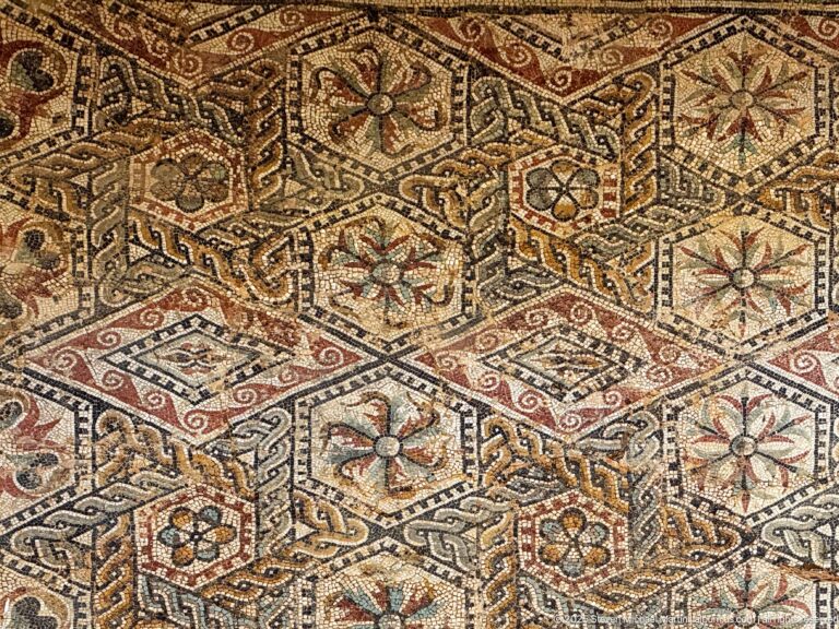 Polychrome Roman mosaic with floral hexagons, interlaced knotwork, and red, ocher, cream, and dark tesserae.