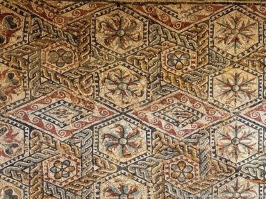 Polychrome Roman mosaic with floral hexagons, interlaced knotwork, and red, ocher, cream, and dark tesserae.