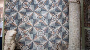 Roman mosaic of repeating eight-pointed stars and circular floral medallions, with part of a marble torso at left.
