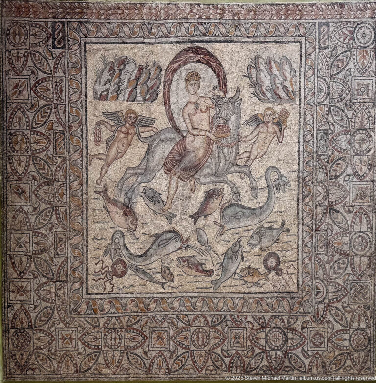 Figurative Roman mosaic with a male rider or hunter surrounded by a lion and other wild animals within ornate borders.