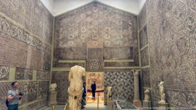Djemila Museum gallery with mosaic-covered walls, a large central marble statue, smaller sculptures, and display cases.