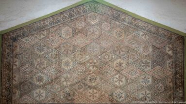 Polychrome Roman mosaic with interlocking octagons, diamonds, stars, and floral rosettes in cream, red, green, and black.