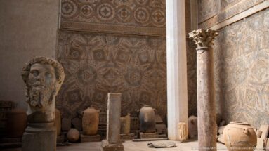 Colossal head of Septimius Severus displayed beside amphorae, a column, and Roman mosaics in Djemila Museum.