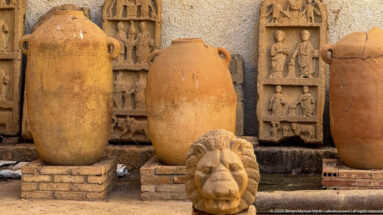 Large Roman amphorae standing before carved relief plaques, with a sculpted lion head in the foreground.