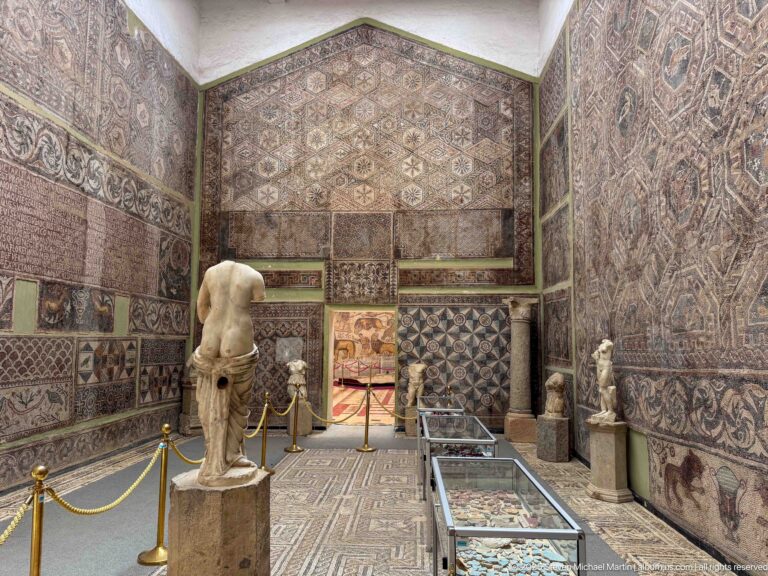 Djemila Museum gallery covered with Roman mosaics, with a headless marble torso, smaller statues, and display cases.