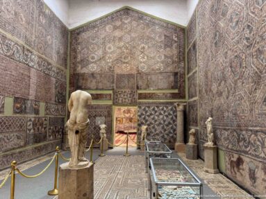 Djemila Museum gallery covered with Roman mosaics, with a headless marble torso, smaller statues, and display cases.