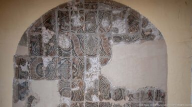 Fragmentary arched Roman mosaic with scrolling geometric patterns and large areas of missing tesserae exposing pale backing.