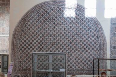 Large arched Roman mosaic covered with tightly repeated scallop motifs in dark, cream, and red tesserae.