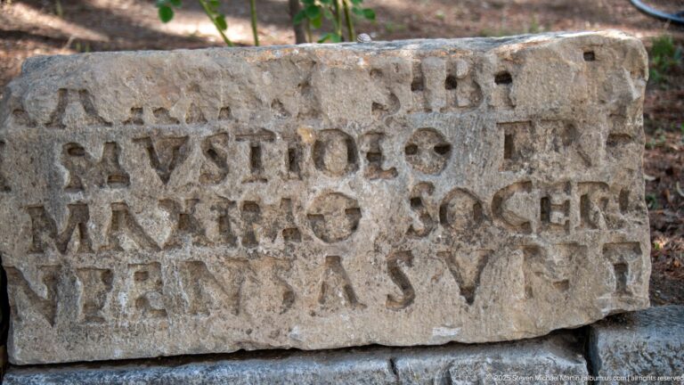 Weathered rectangular stone block with several lines of deeply carved Latin capital letters.