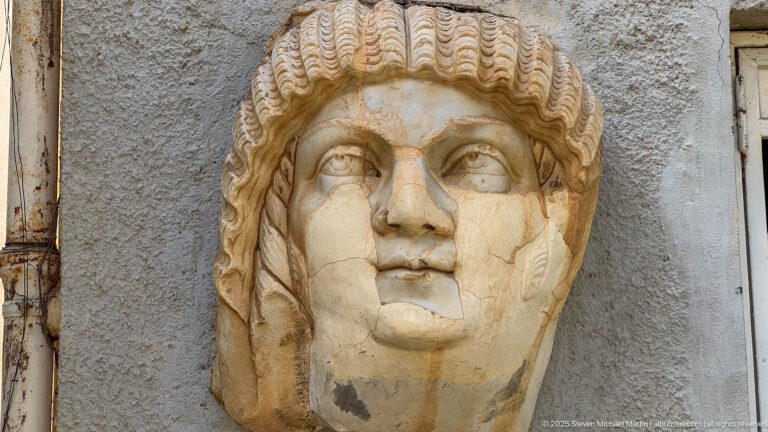 Marble Roman portrait head of a youthful man with short patterned curls and visible surface cracks.