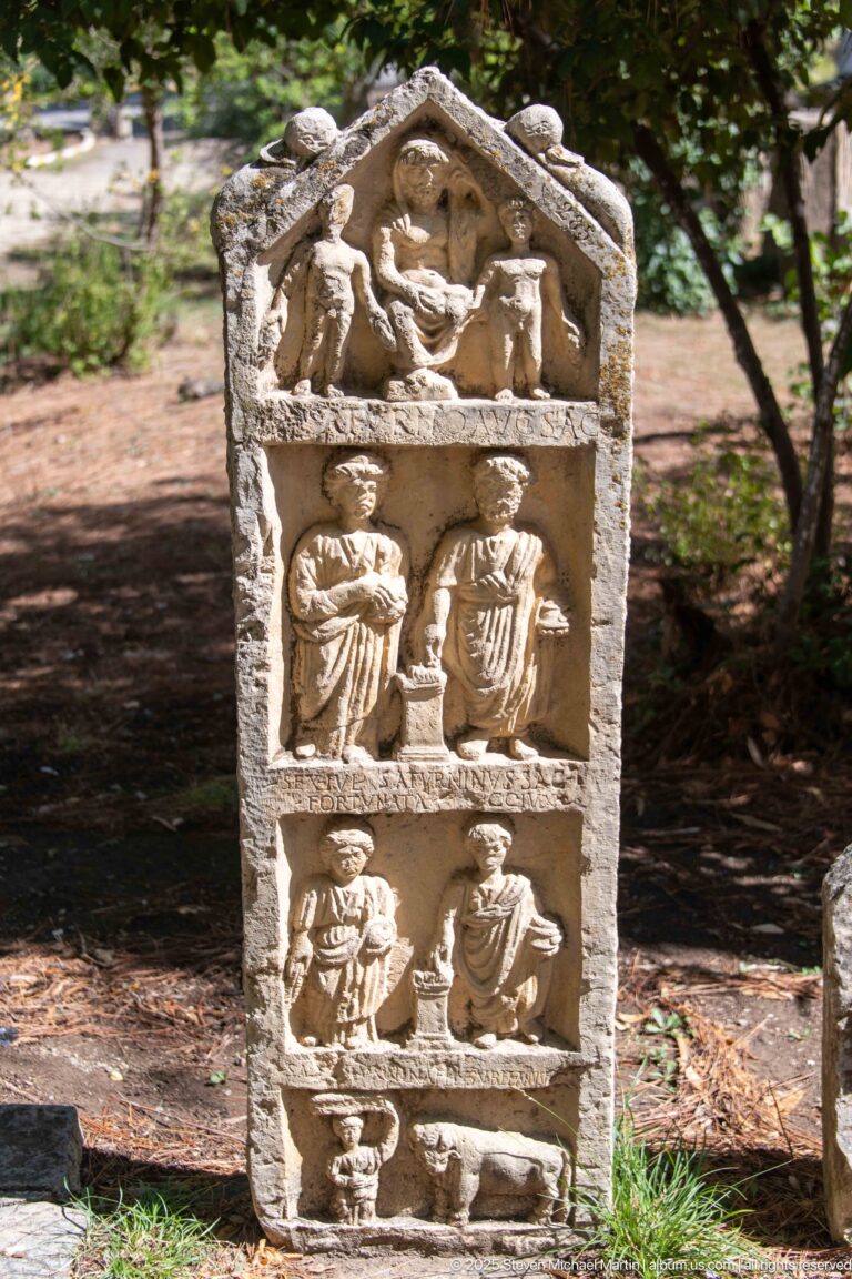 Carved stone stele with stacked relief panels showing multiple human figures beneath a triangular top.