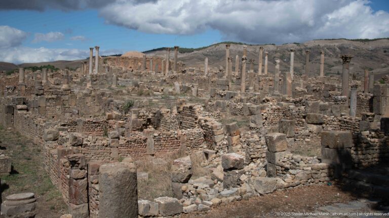 Mixed brick-and-stone Roman walls and rubble with standing columns across the upper ruins at Djemila.