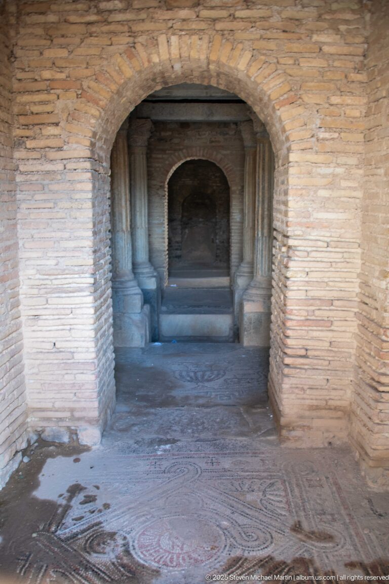Axial view through brick arches across a geometric mosaic floor toward a darker inner chamber.