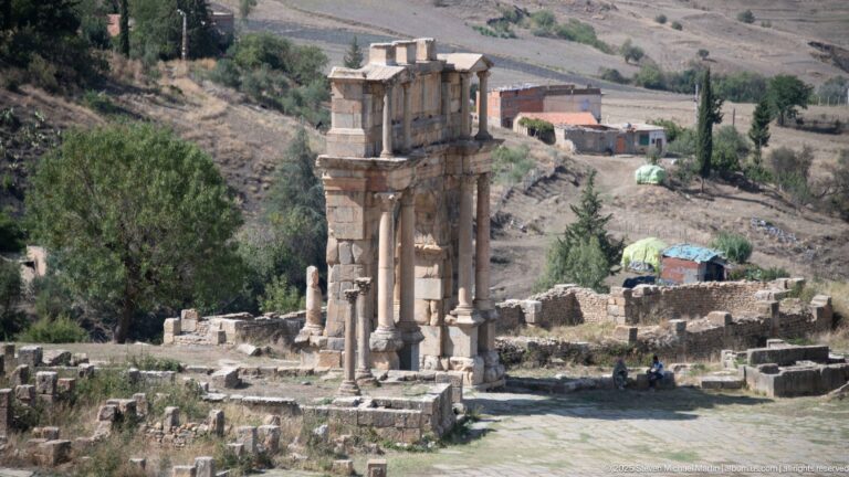 Monumental Roman triumphal arch with tall central opening, side bays, and columns among the ruins of Djemila.