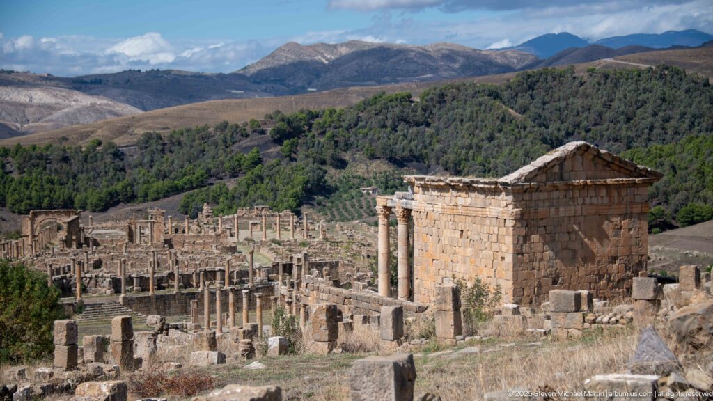 Rectangular Roman stone building with triangular pediment standing above columns and ruins at Djemila.