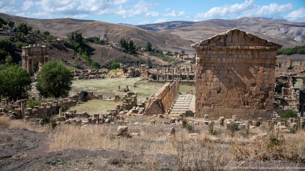 Large Roman temple on a high podium with pediment, columns, and steps amid the ruins of Djemila.