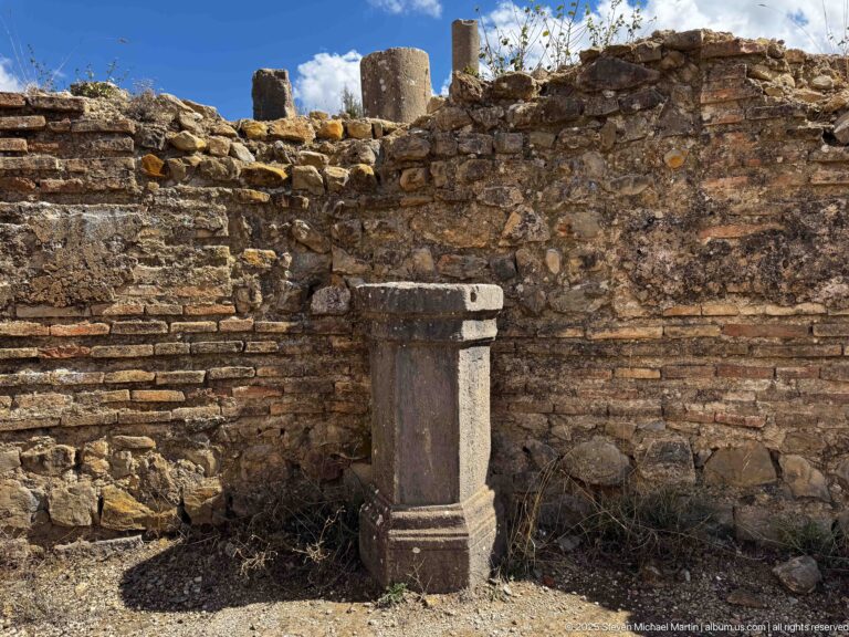 Small molded stone pedestal before a weathered Roman wall of mixed stone and brick courses.