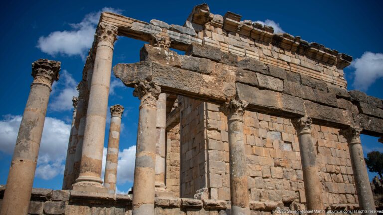 Low-angle detail of Roman temple columns, carved capitals, entablature, and stone cella at Djemila.