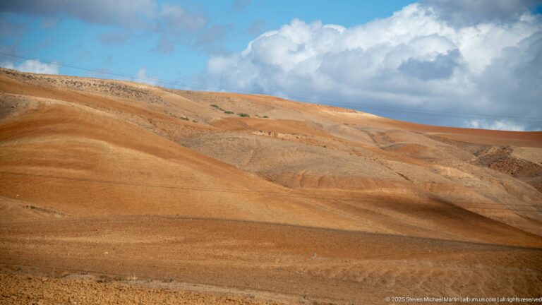 Rust-colored eroded hills beneath bright clouds in the uplands around Djemila.