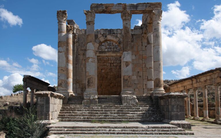Frontal view of a Roman temple façade with broad steps, tall columns, and a blocked central doorway.