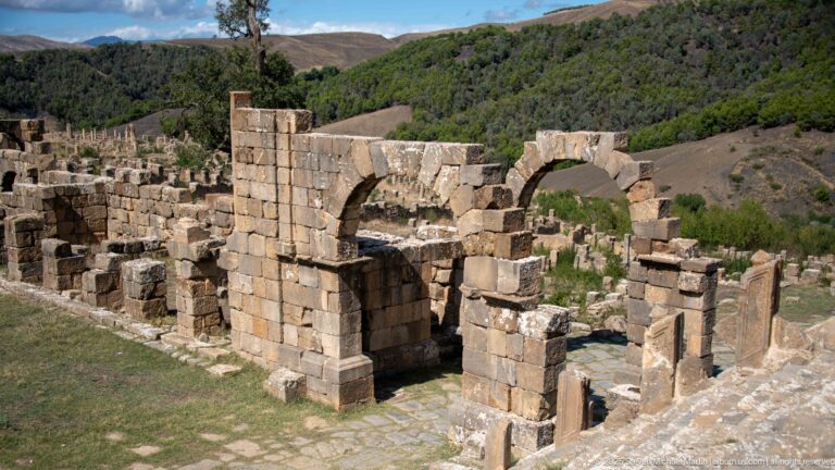 Roofless Roman masonry structure with several arched openings and thick stone walls at Djemila.