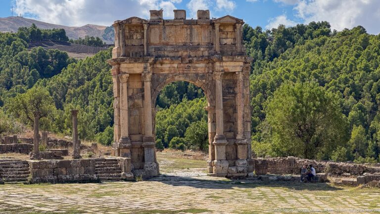 Frontal view of Djemila's Roman triumphal arch with central opening framing woodland beyond.