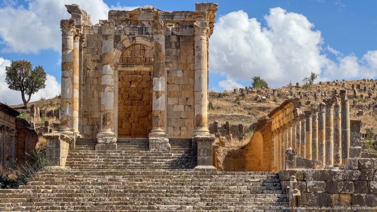 Roman temple façade above broad steps with a long adjoining colonnade extending to the right at Djemila.