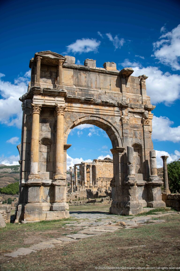 Close oblique view of a monumental Roman triumphal arch with paired columns and heavy upper masonry at Djemila.