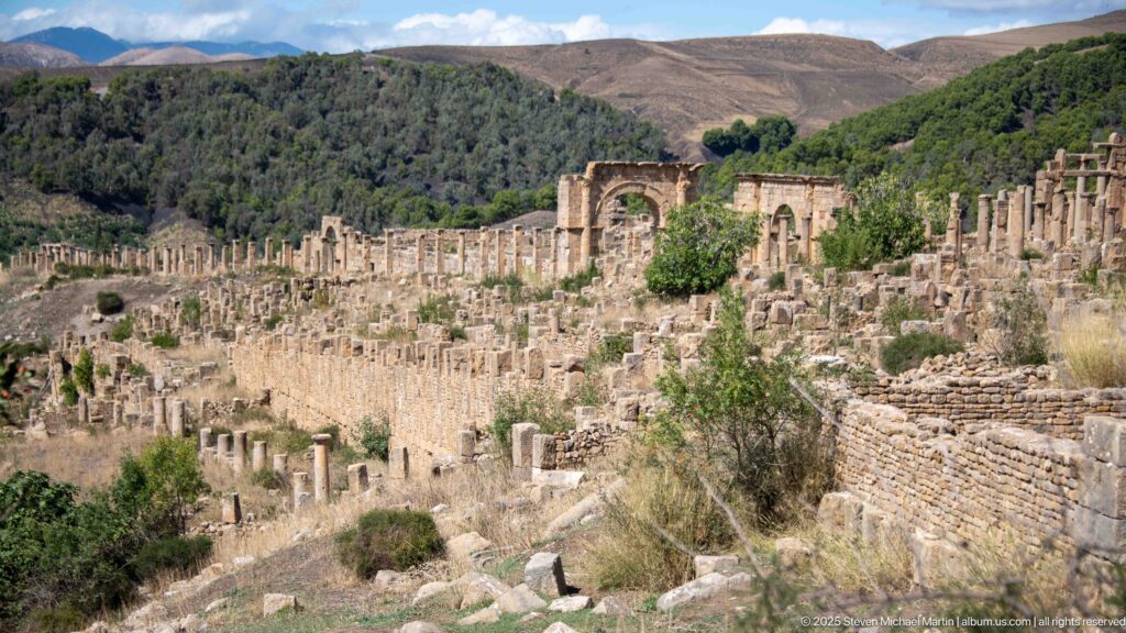 Wide elevated view of Djemila with dense Roman columns, walls, arches, and mountain slopes beyond.