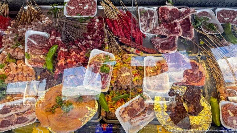 Market table crowded with butchered meat, peppers, spices, prepared foods, and packaged items near Djemila.