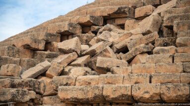 Large rectangular stone blocks collapsed across a damaged section of the Medracen’s stepped masonry, with intact courses surrounding the break.