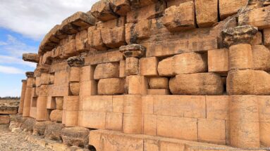 Raking view along the curved Medracen wall showing repeated engaged columns, dressed block panels, and weathered projecting stonework.