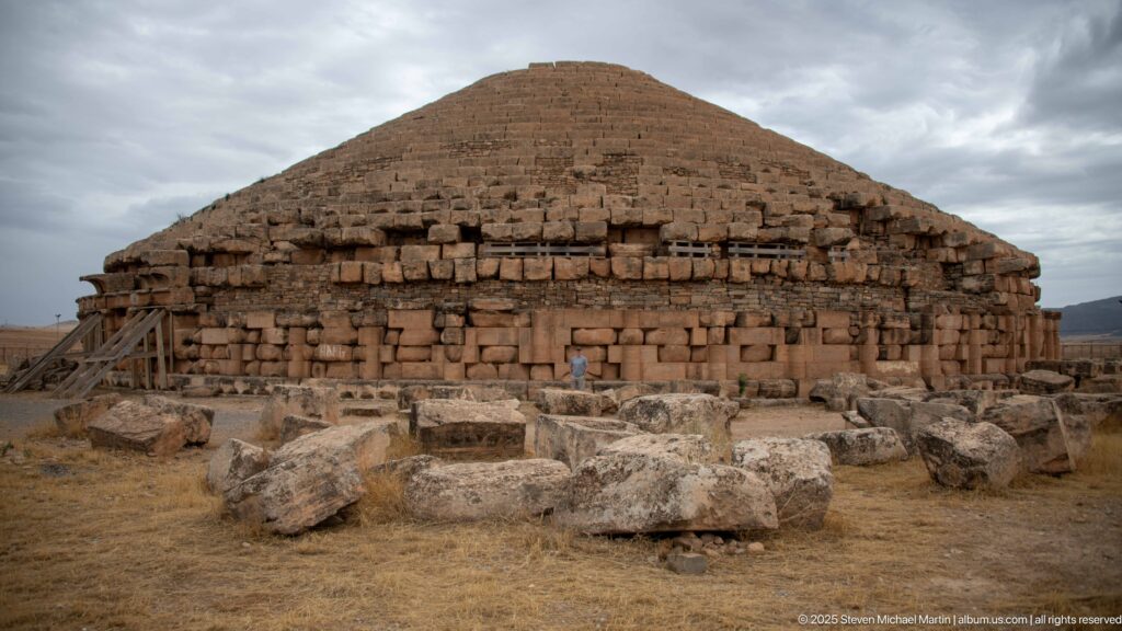 Centered frontal view of the Medracen’s circular stone body and stepped conical roof, with fallen blocks and timber braces.