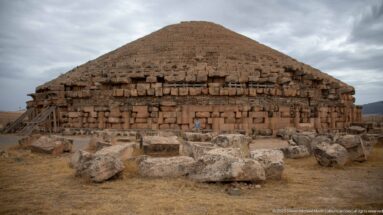 Centered frontal view of the Medracen’s circular stone body and stepped conical roof, with fallen blocks and timber braces.