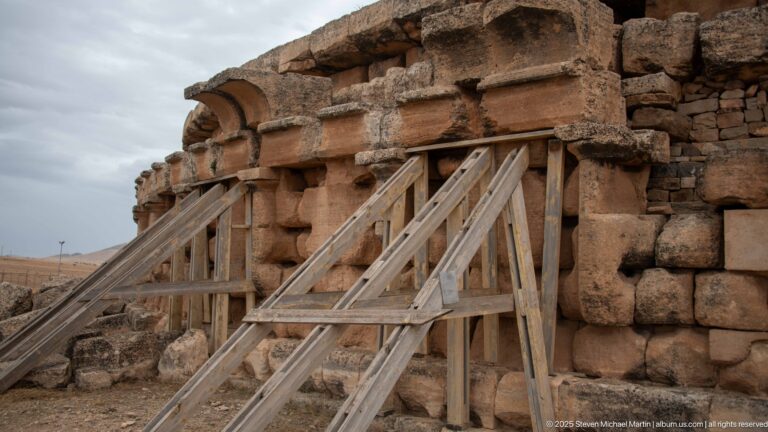 Timber shoring bracing damaged stonework on the Medracen, beneath projecting blocks and a semicircular recessed architectural feature.