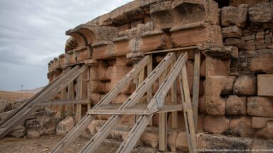 Timber shoring bracing damaged stonework on the Medracen, beneath projecting blocks and a semicircular recessed architectural feature.