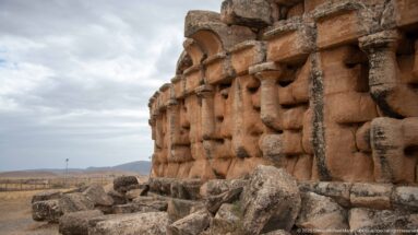 Low oblique view along the Medracen wall with projecting stonework, semicircular recesses, weathering, and fallen blocks at the base.