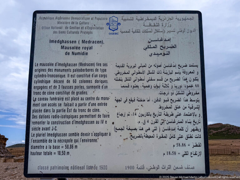 French-Arabic interpretive panel for Medracen with the mausoleum visible in the background beneath a cloudy sky.