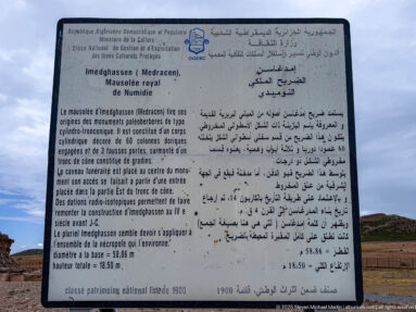 French-Arabic interpretive panel for Medracen with the mausoleum visible in the background beneath a cloudy sky.