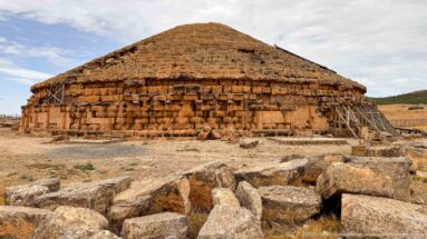 Fallen stone blocks before the circular Medracen mausoleum, with stepped roof, dressed masonry, and timber stabilization supports.