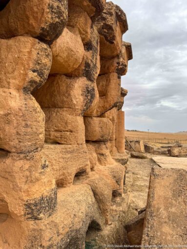 Oblique close-up of weathered projecting stone blocks on the Medracen exterior, with erosion, dark staining, and open joints.