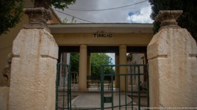 Entrance gate to Timgad with masonry piers, metal barriers, and a portico labeled TIMGAD.