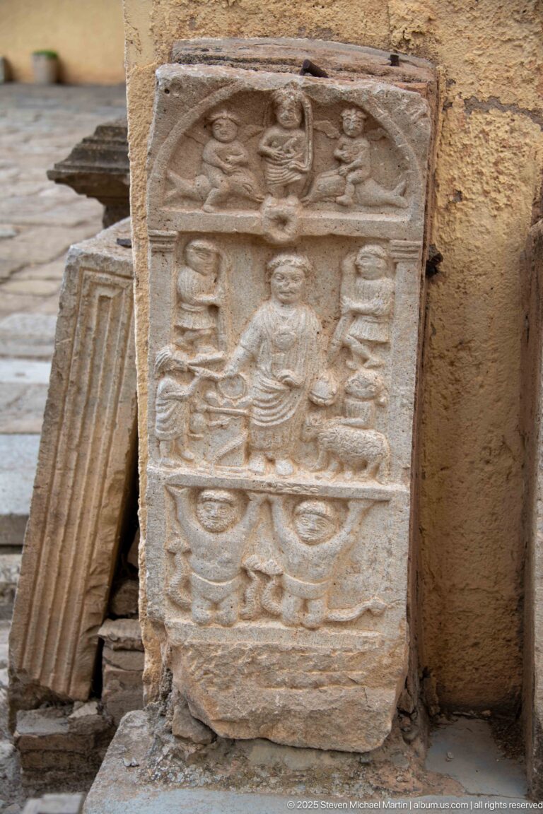Weathered stone stele with a seated central figure and multiple carved symbolic motifs arranged in registers.