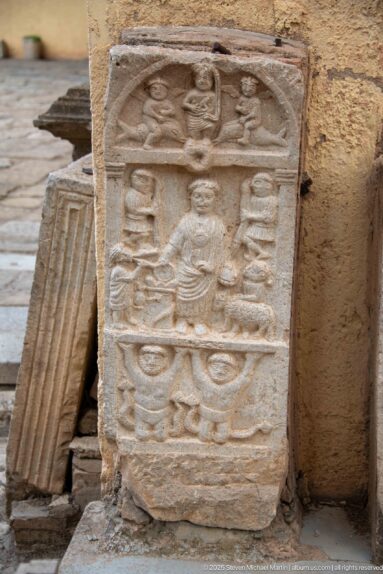 Weathered stone stele with a seated central figure and multiple carved symbolic motifs arranged in registers.