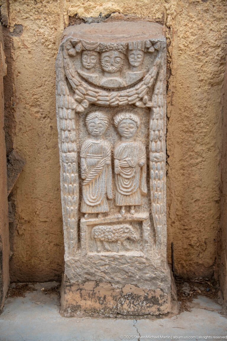 Stone stele with paired central forms, circular and crescent motifs above, and beaded vertical borders.