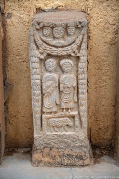 Stone stele with paired central forms, circular and crescent motifs above, and beaded vertical borders.