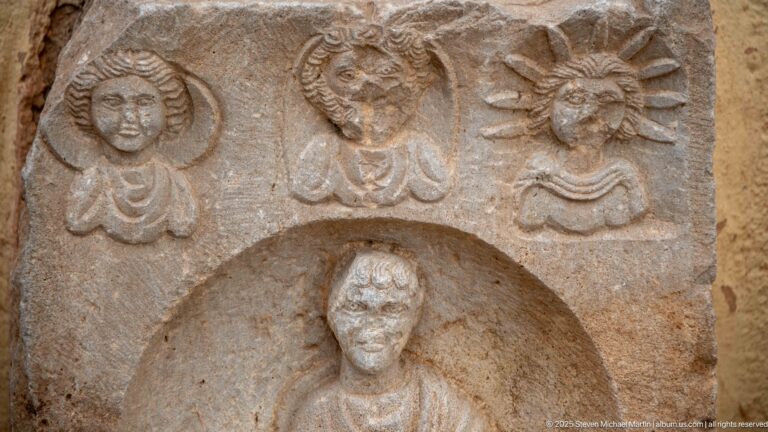 Close detail of a stone stele with three carved busts above a larger figure in a recessed niche.
