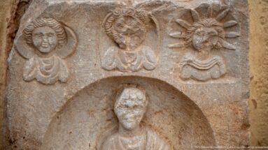Close detail of a stone stele with three carved busts above a larger figure in a recessed niche.