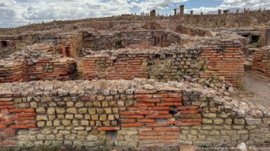 Ruined Roman walls built of rubble stone and red brick, with exposed rooms and layered masonry.
